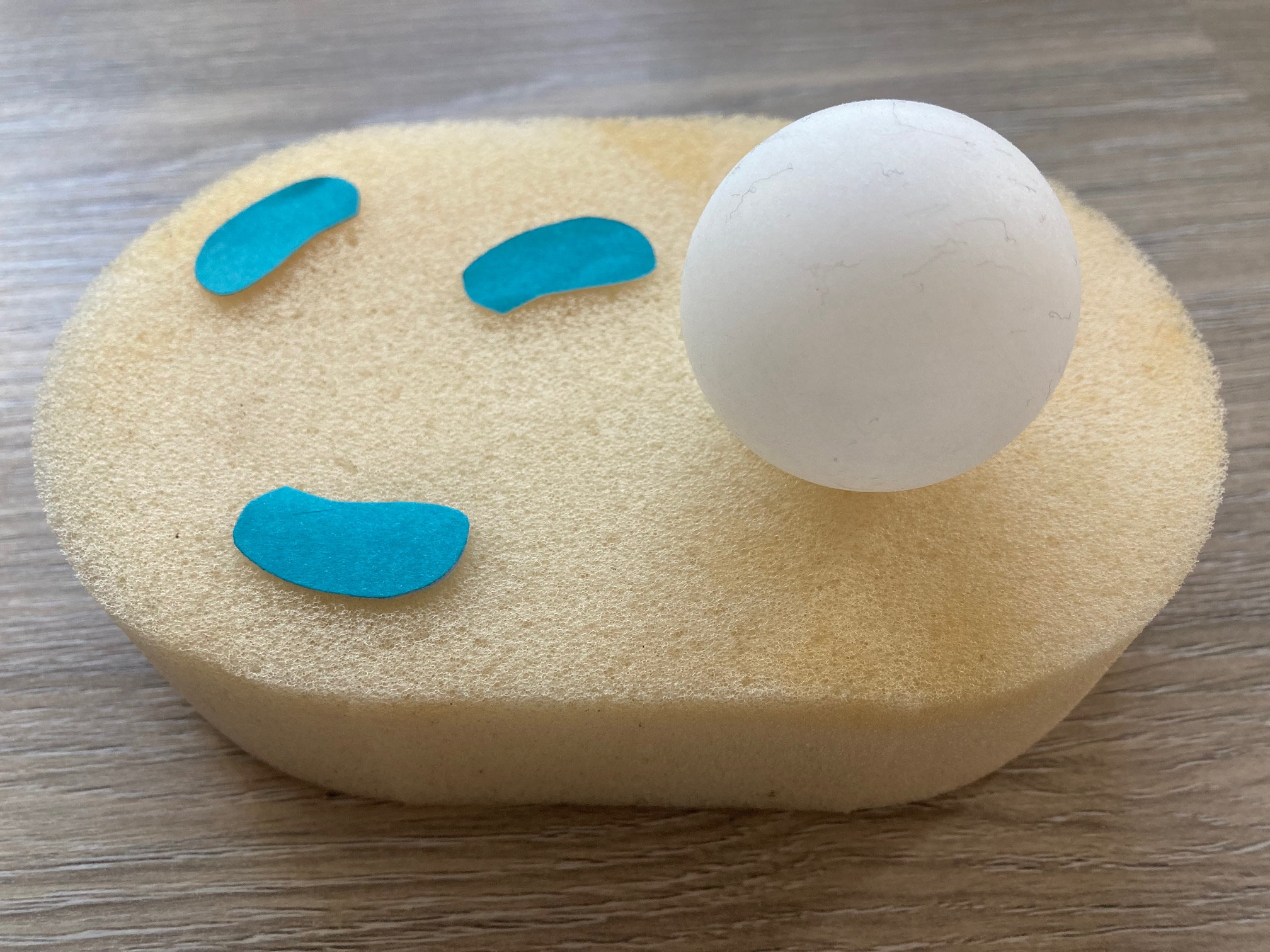 a white egg sitting on top of a wooden table next to a blue piece of paper on top of a wooden table