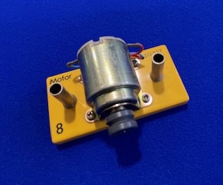 a motor on a blue surface with a yellow board and two black knobs on the front of the motor